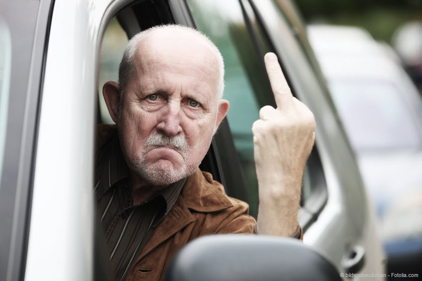 Mann fährt Auto und zeigt Handzeichen mit Mittelfinger